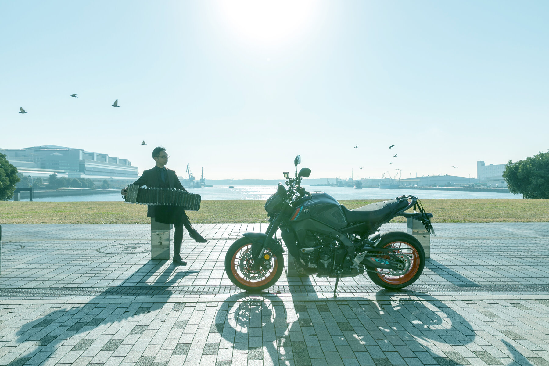 港の風景の中、バンドネオンとバイクとともに立つ早川純