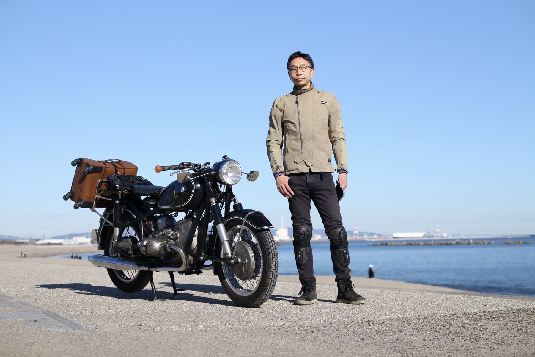 海辺で旧車のバイクの隣に立つ早川純